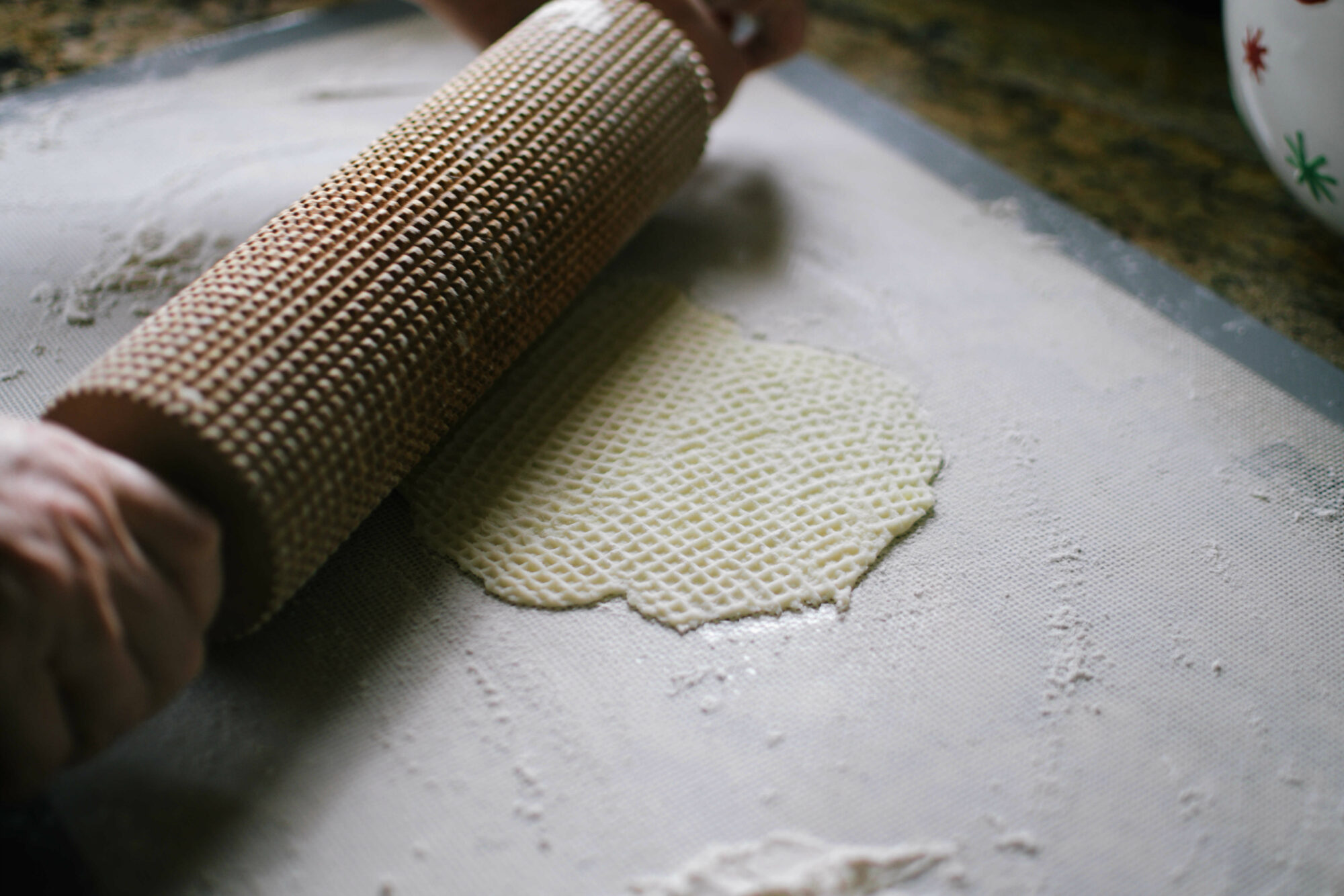 A side image of a closeup of a woman rolling lefse dough on a white counter.