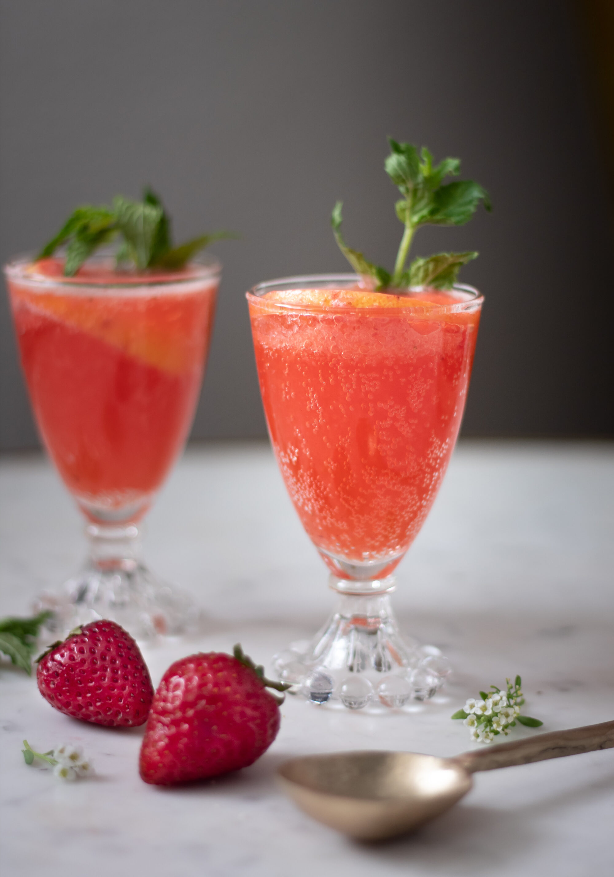 A closeup of two glasses of sparkling strawberry bourbon lemonade with mint on a white counter.