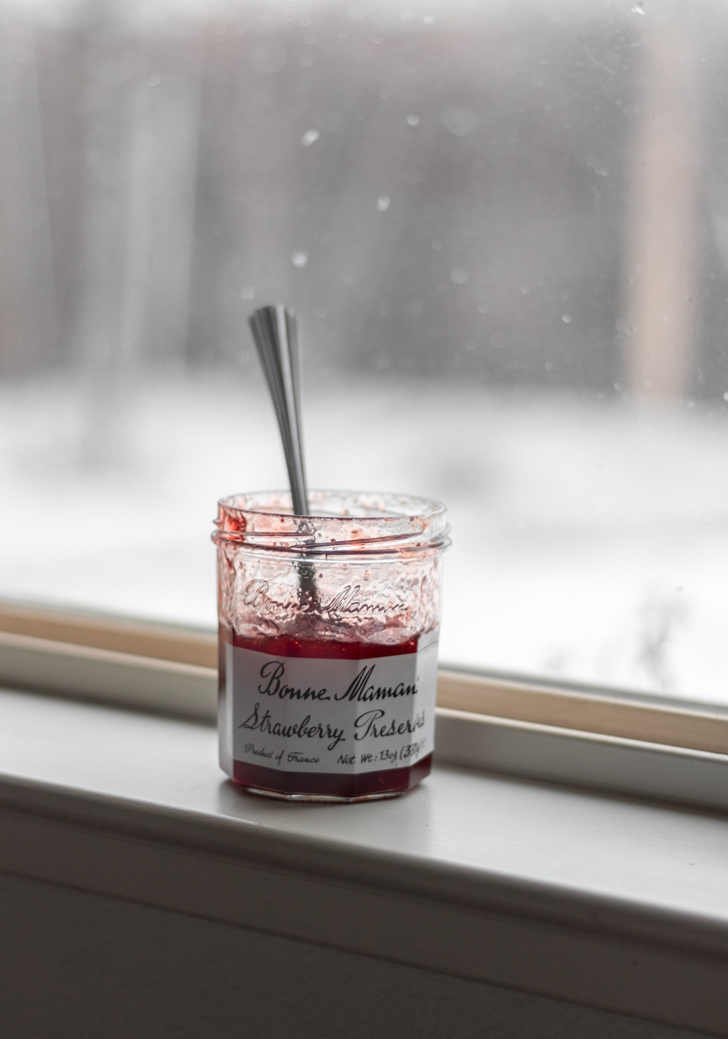 A jar of Bonne Maman preserves on a window sill with a snowy scene in the background.