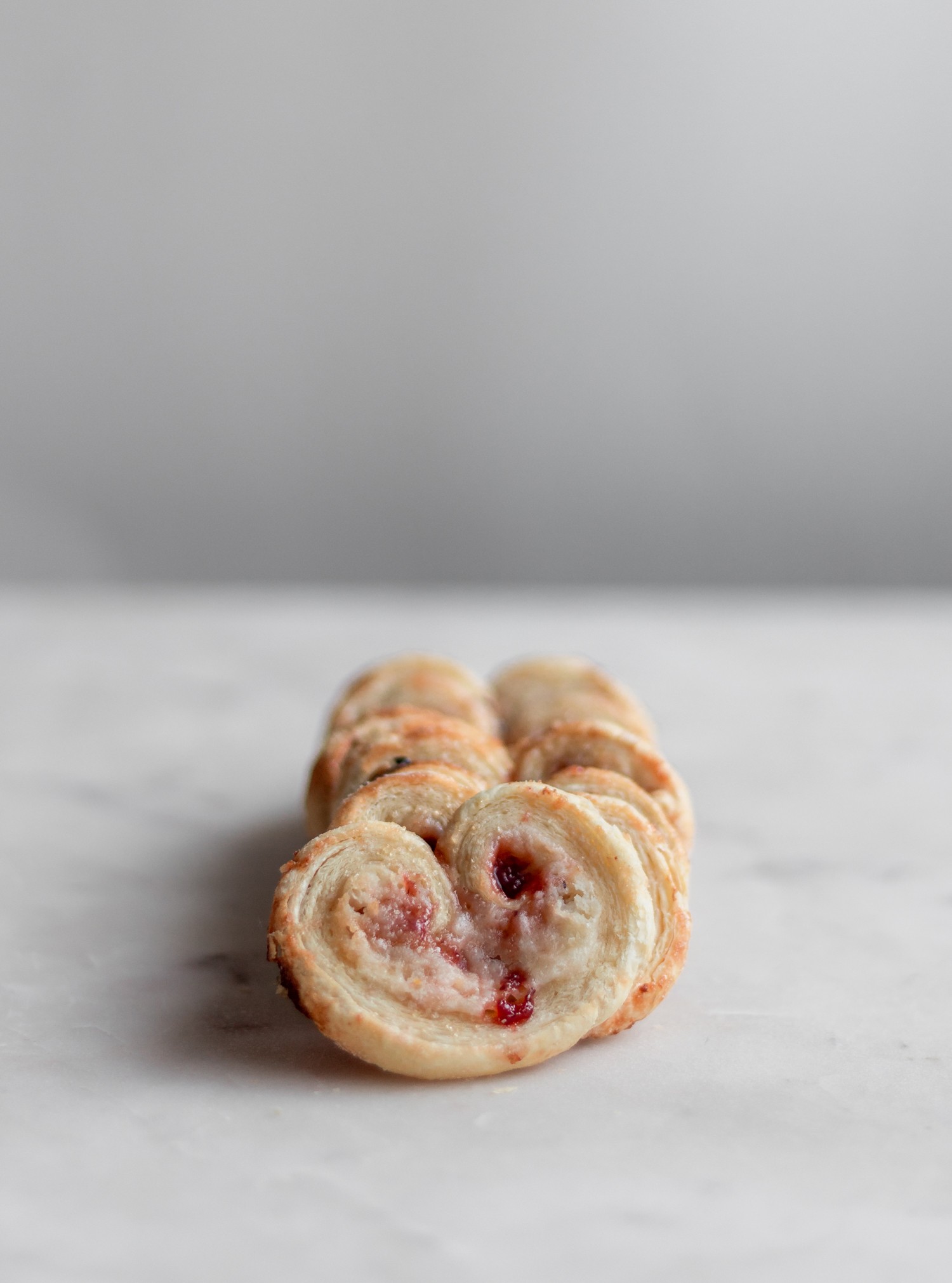 A closeup side image of a row of strawberry palmiers on a white marble table.