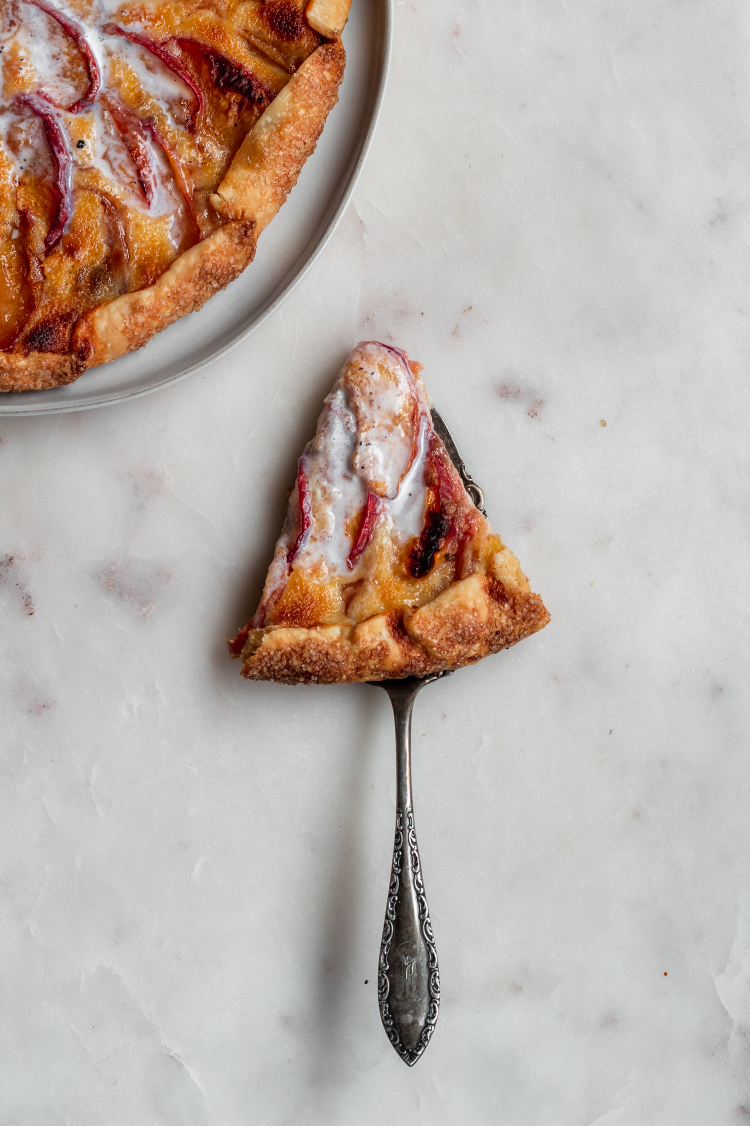 An overhead image of a pie server with a slice of peach crostada on a marble counter.