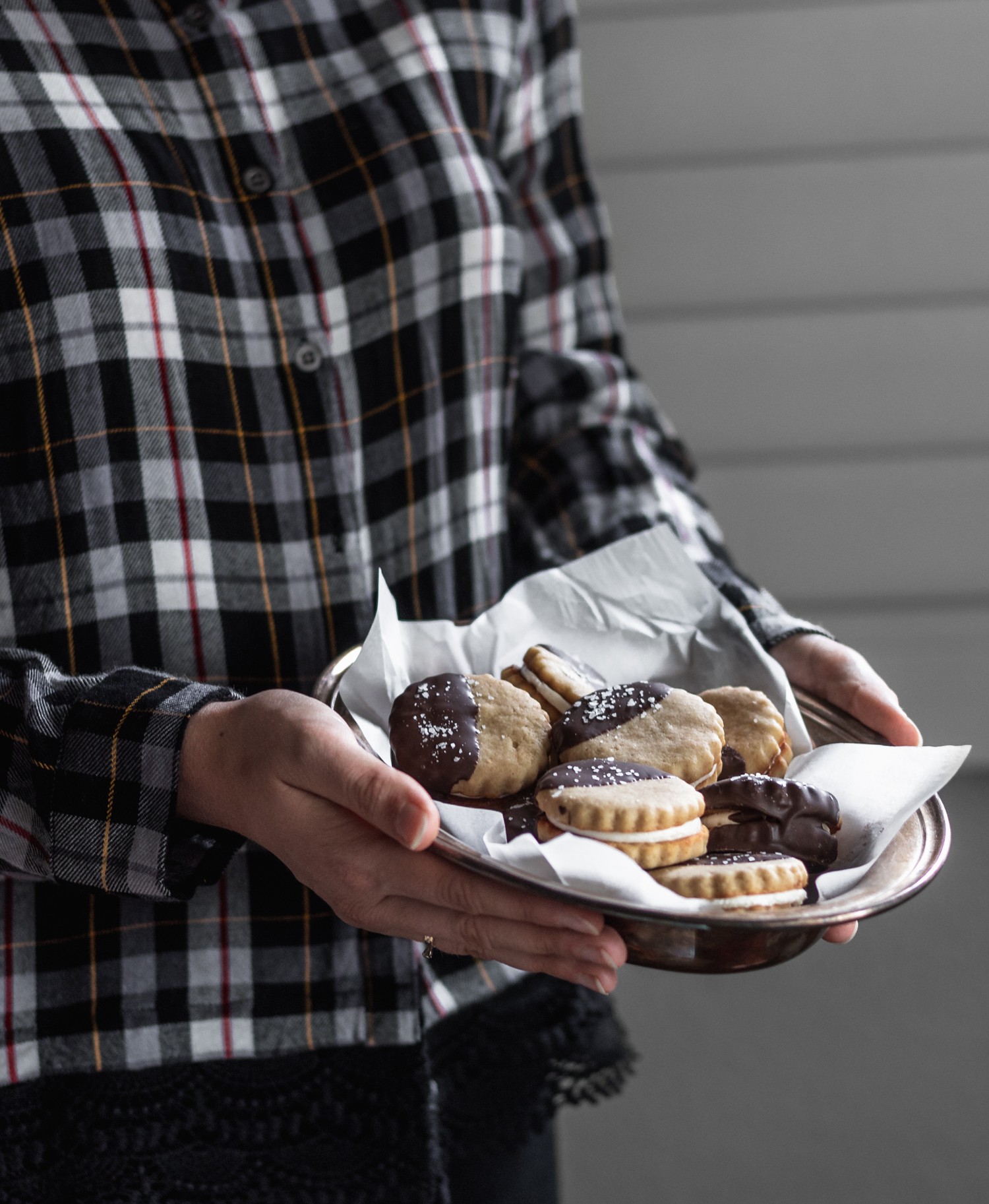 A woman wearing a black flannel shirt holding a metal dish of s'mores sandwich cookies.