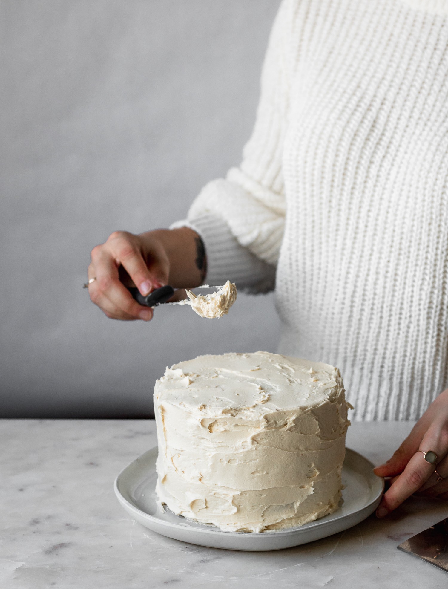 A woman wearing a white sweater frosting a layer cake.
