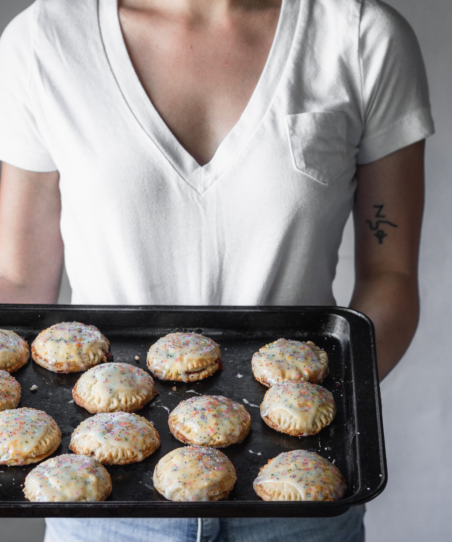 A woman holding a sheet pan with strawberry balsamic hand pies.