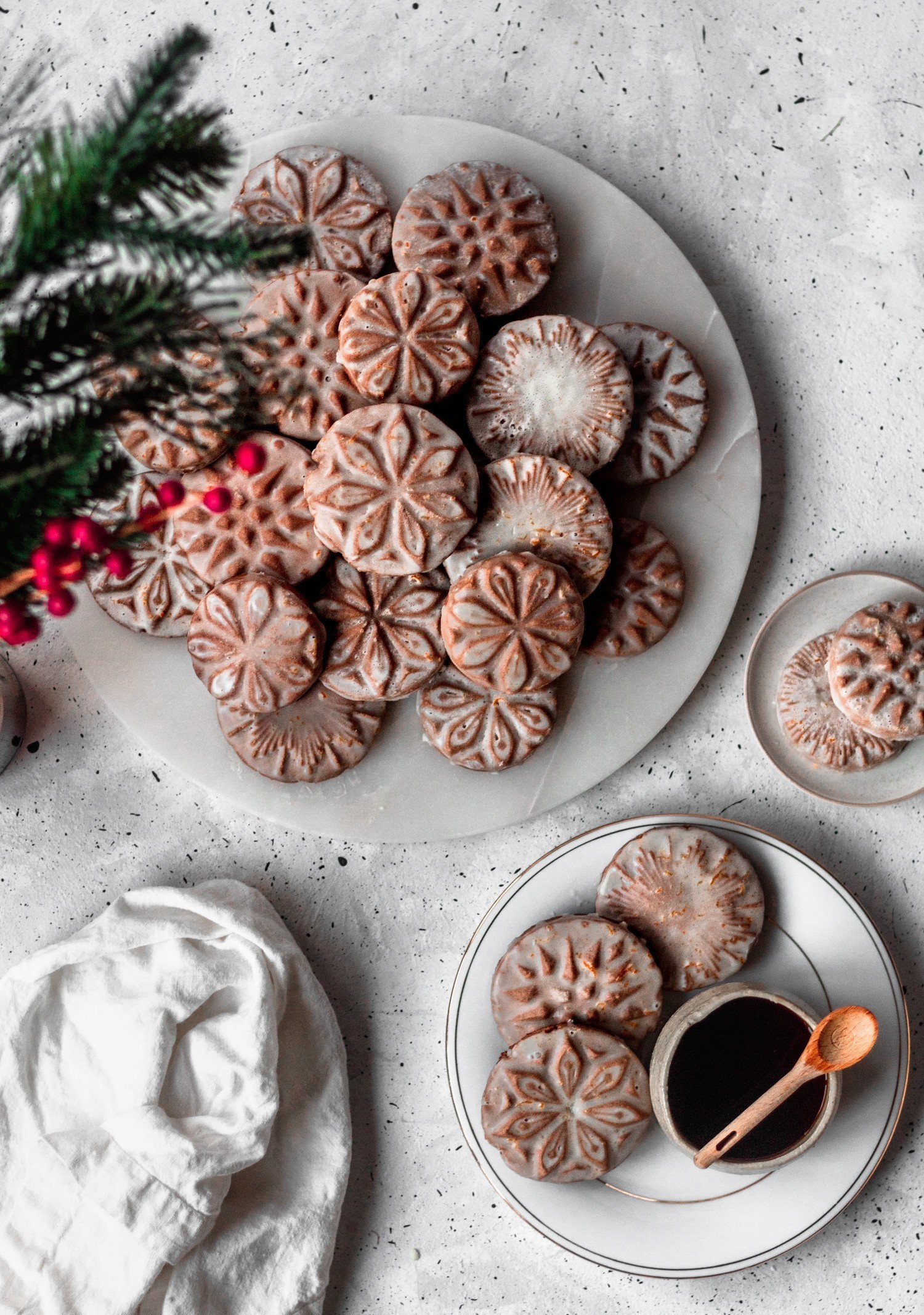 An overhead image of cardamom gingerbread cookies on a white marble plate on a grey table surrounded by smaller plates of cookies.