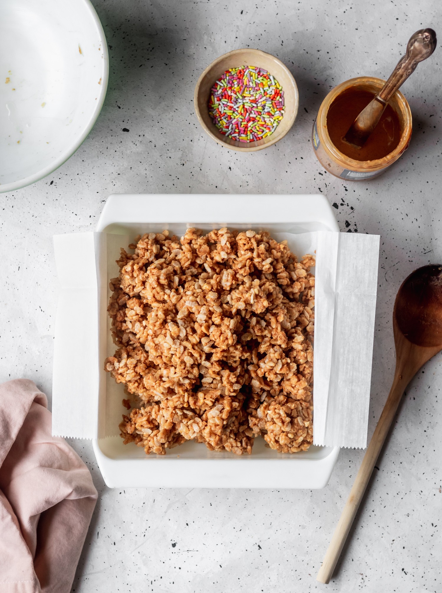 A white baking dish filled with nutty, crispy cereal dessert on a grey background.