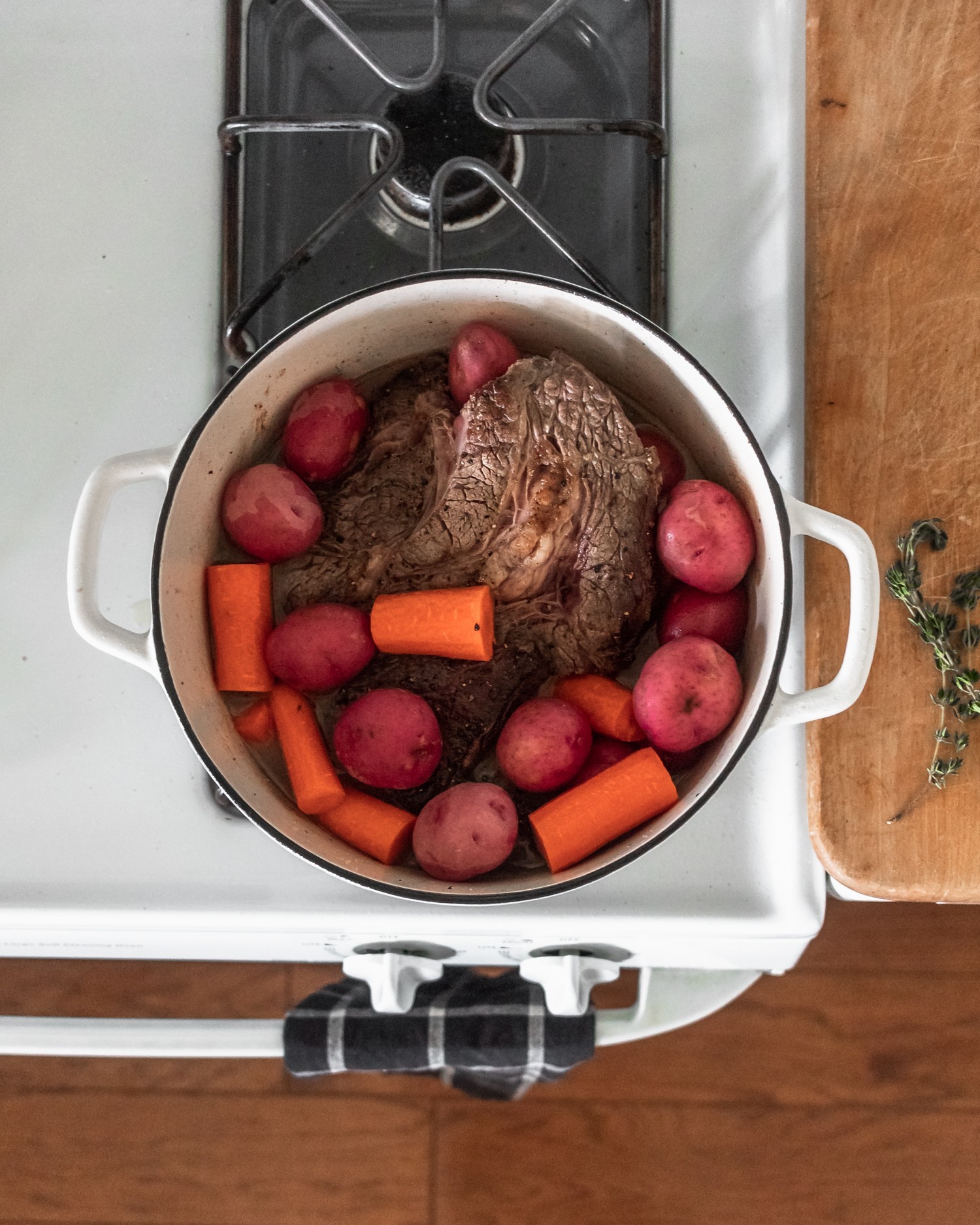 A Dutch oven filled with beef, potatoes, and carrots on a white stove.