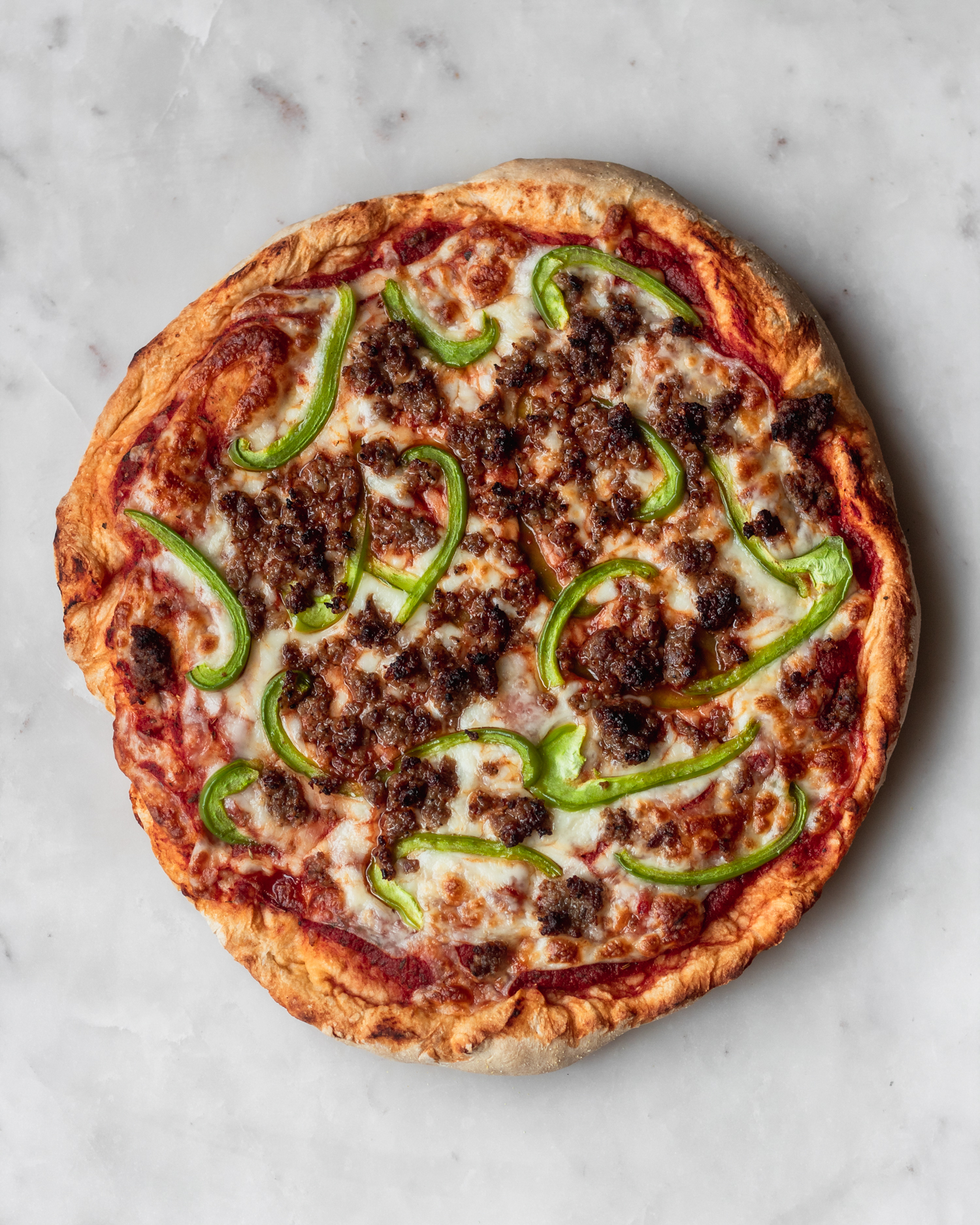 A bird's eye view of homemade pizza, one of my favorite pantry staple meals, with sausage and green peppers on a white marble background.