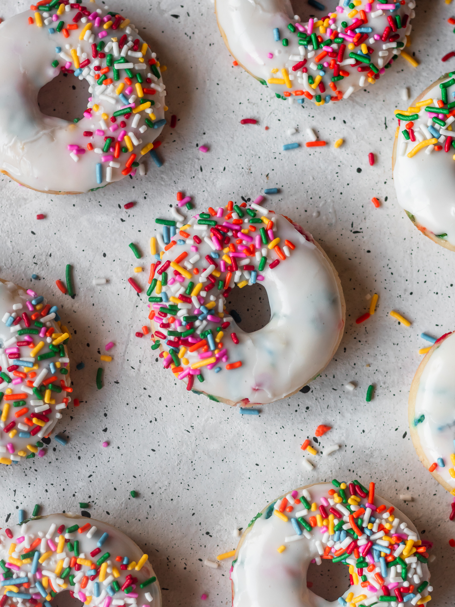An closeup overhead shot of birthday cake donuts on a grey table.