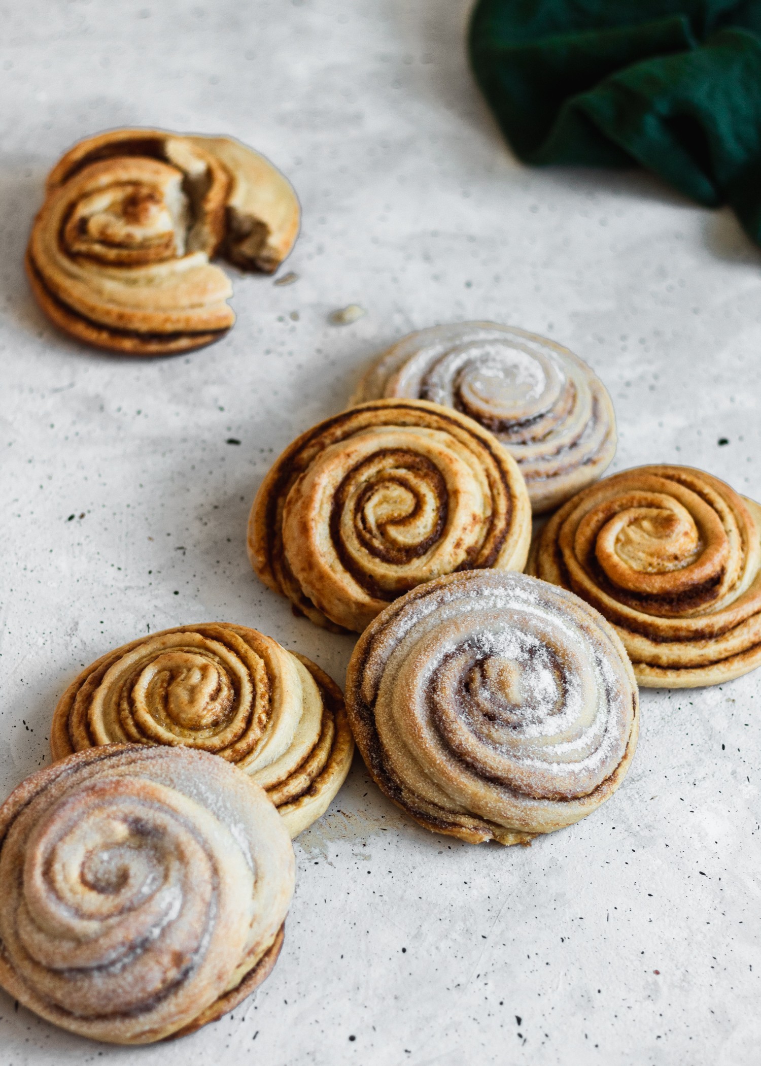 A side shot of cinnamon rolls on a white table with a green linen in the background.