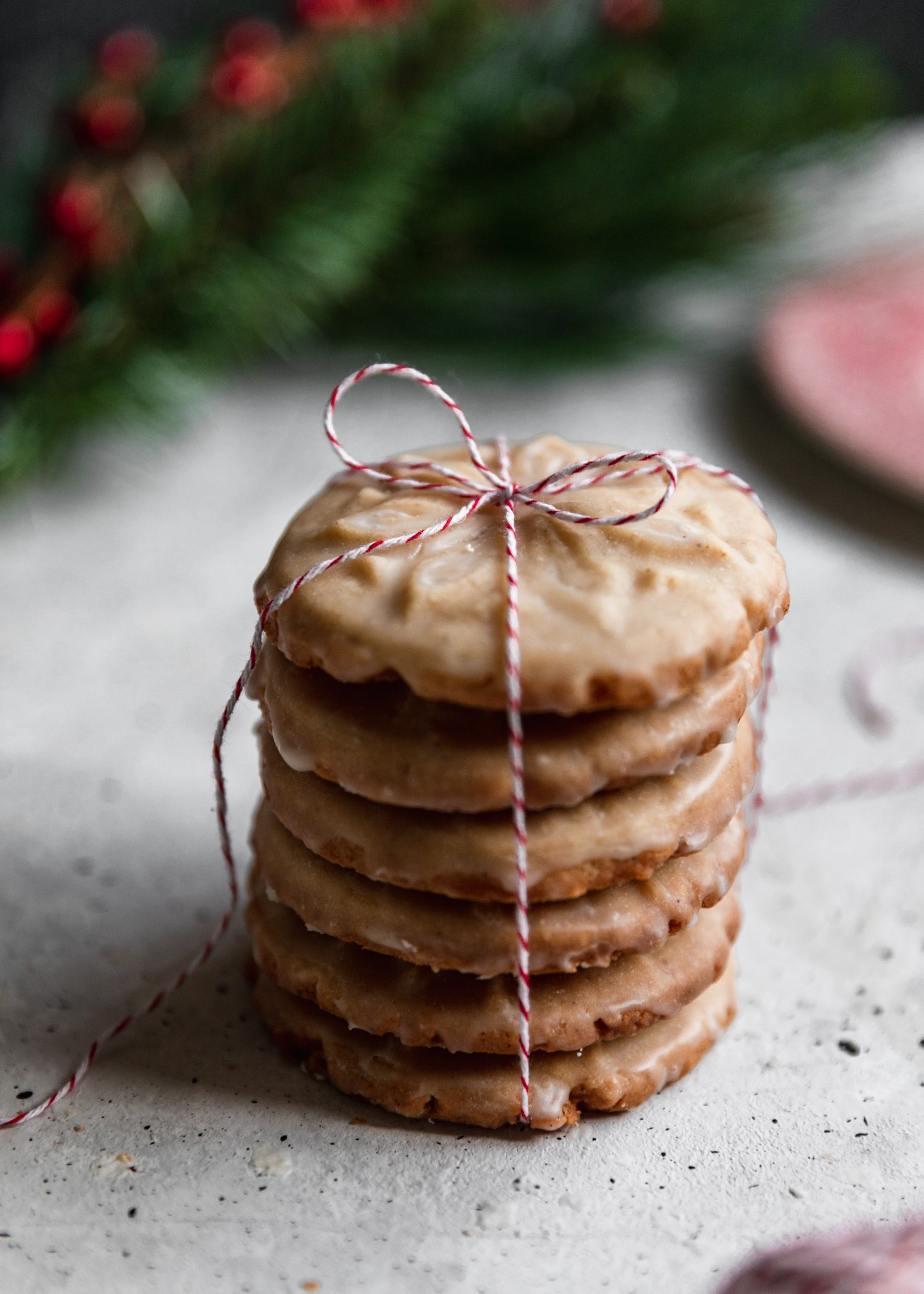 A side image of a stack of eggnog cookies tied with string on a white background with green pine branches and a red plate in the background.