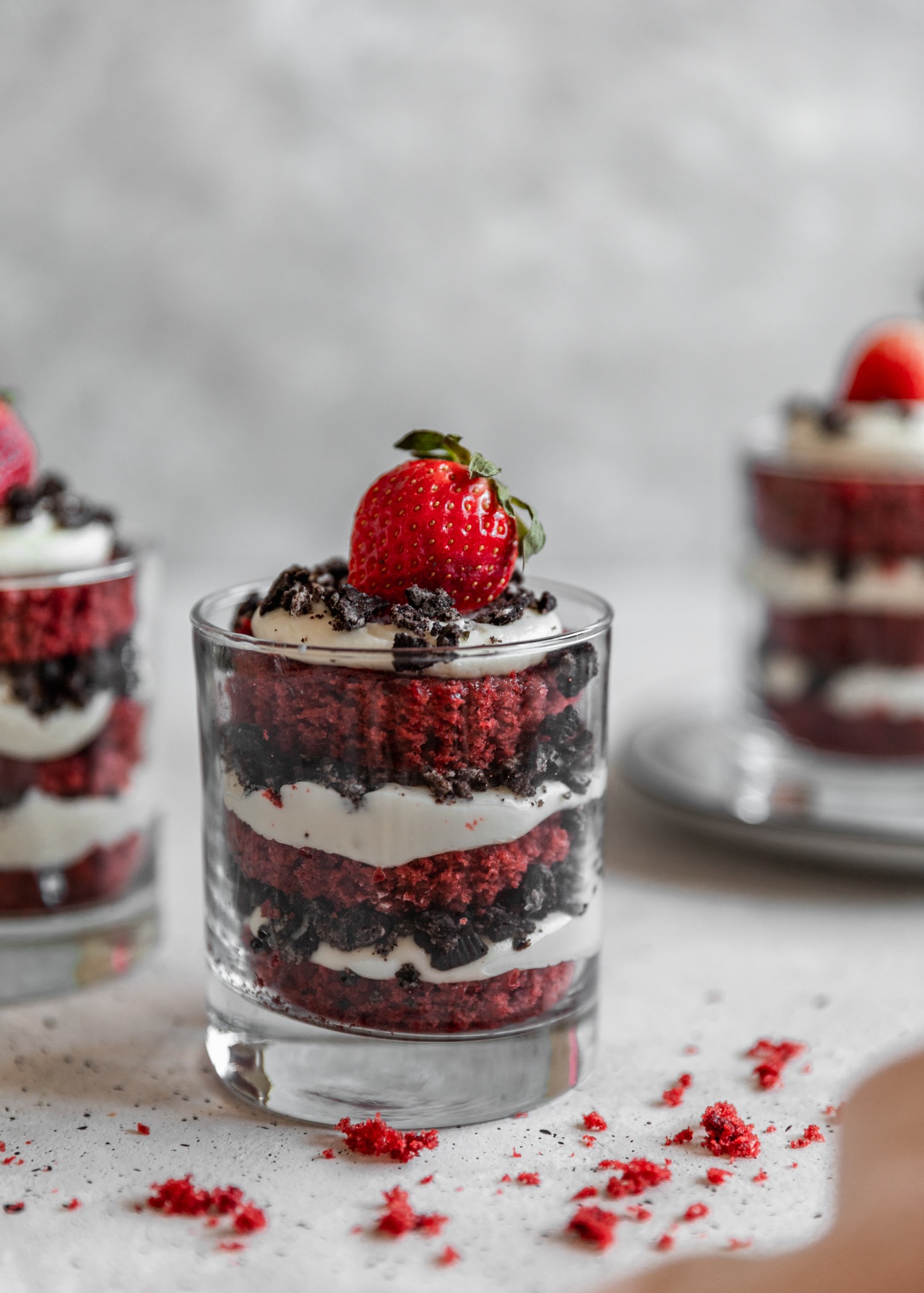 A closeup side shot of three red velvet trifles on a speckled white table.