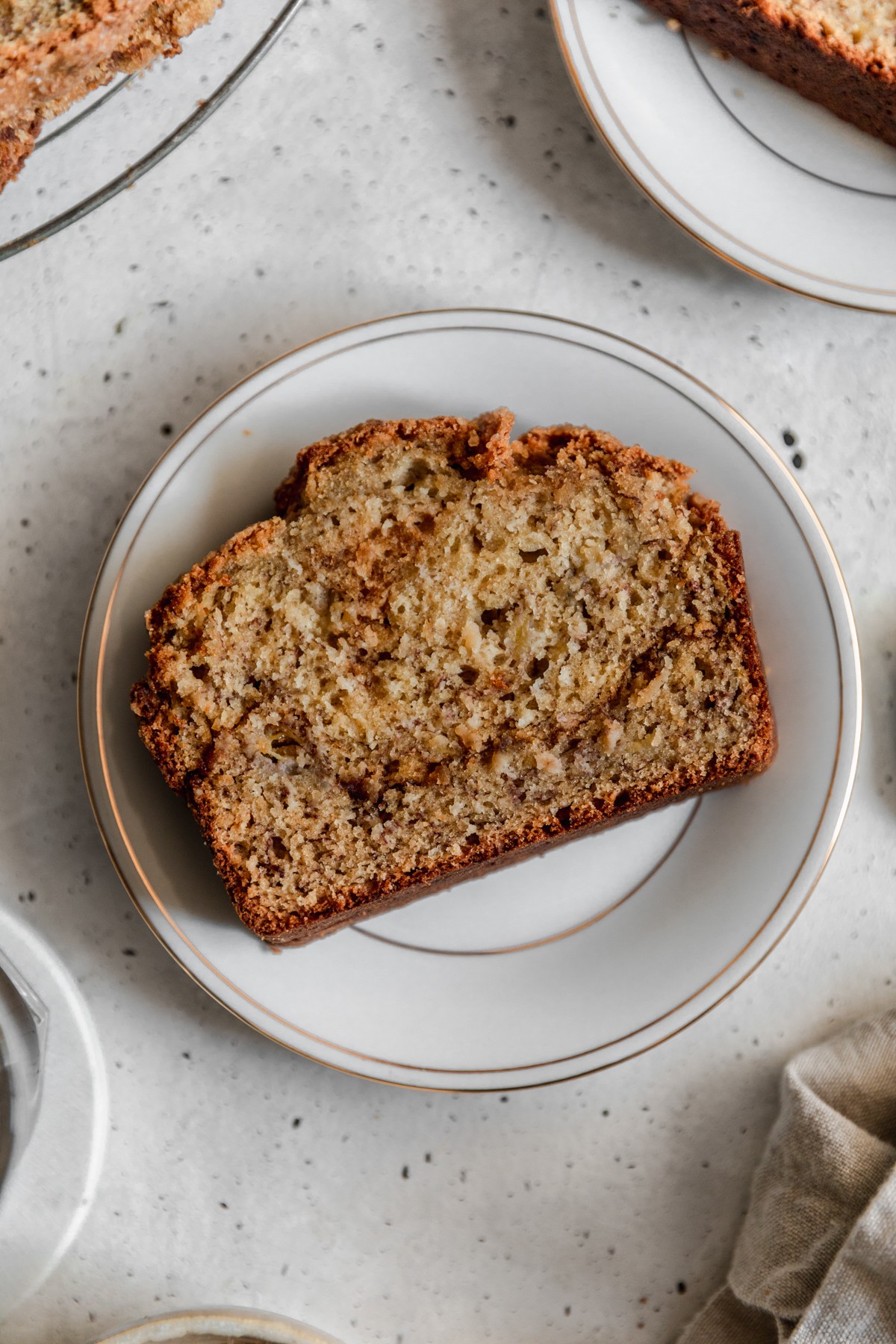 A close-up image of a white plate with a slice of cookie butter banana bread on a grey table.