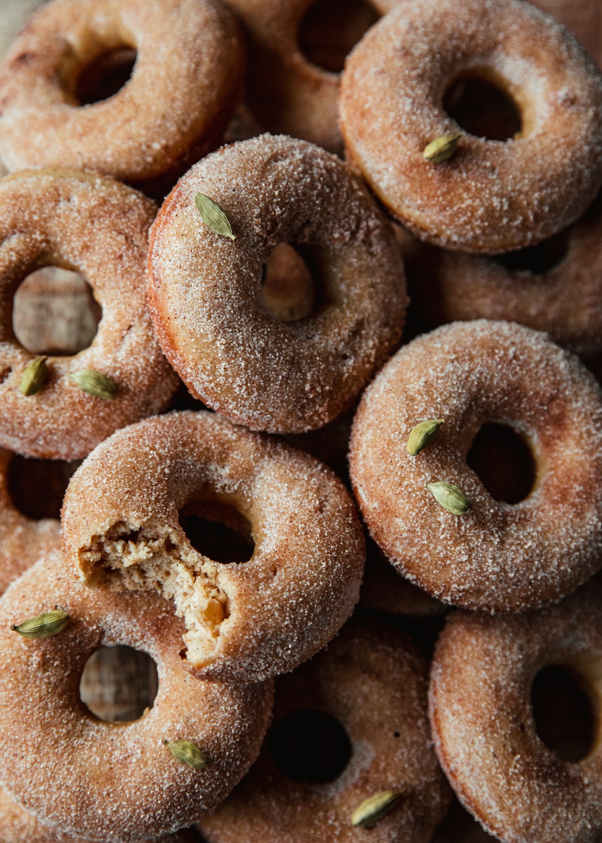 A very closeup overhead image of a stack of apple cider donuts topped with cardamom pods.