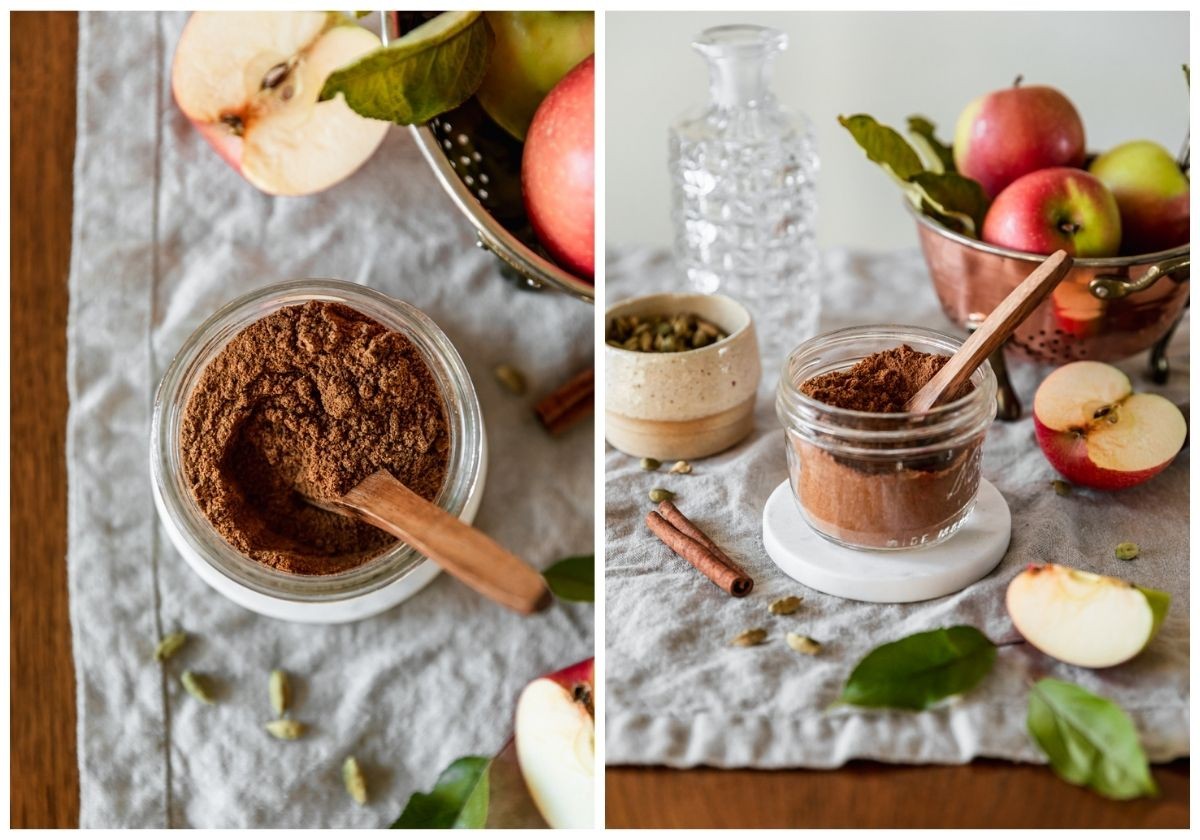 Two images; on the left, a closeup overhead image of spices in a jar on a beige linen next to sliced apples, a colander with apples, cardamom, and a cinnamon stick. On the right, a side image of the jar of spices on a white coaster placed on a beige linen next to a copper colander with apples, sliced apples, a cream bowl of cardamom pods, and a glass container.
